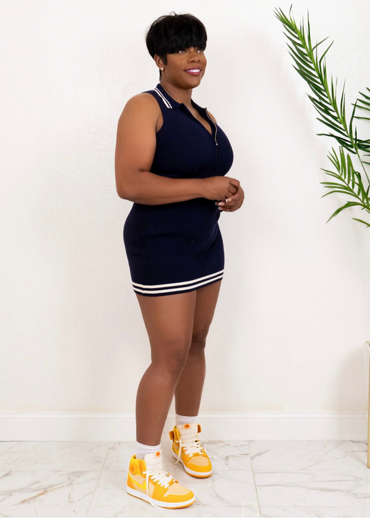 Angled view of navy ribbed zip-front mini dress with sleeveless fit and stripe trim, styled with yellow Nike sneakers.