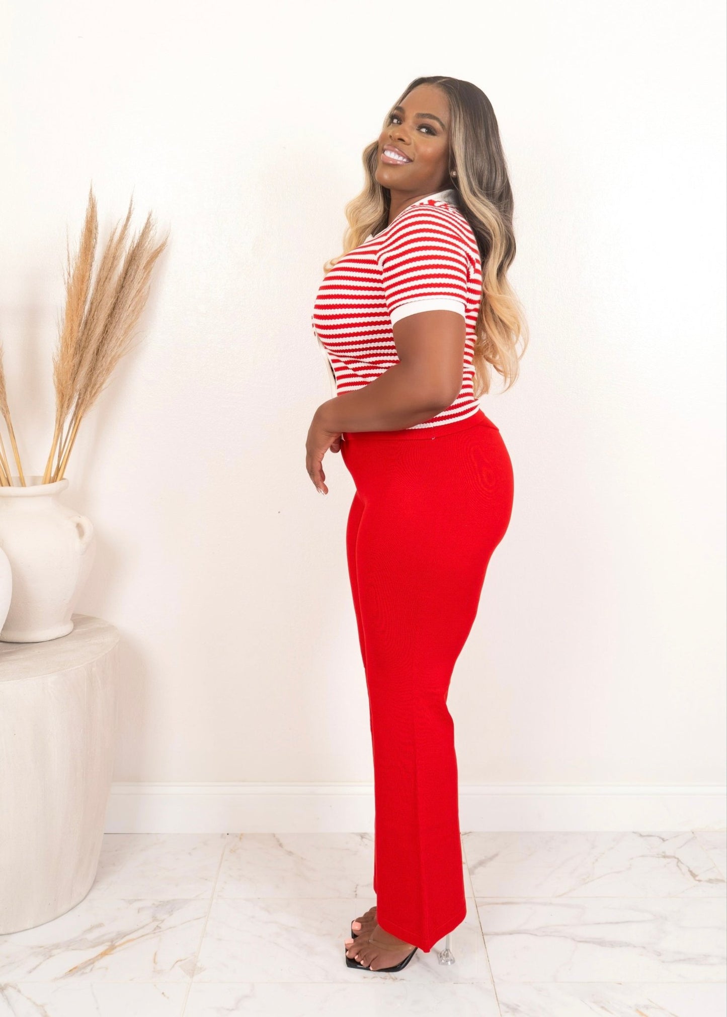 Side view of model wearing red high-waisted flare pants and cropped red-and-white striped cardigan with heels. Curvy summer  set outfit for women.
