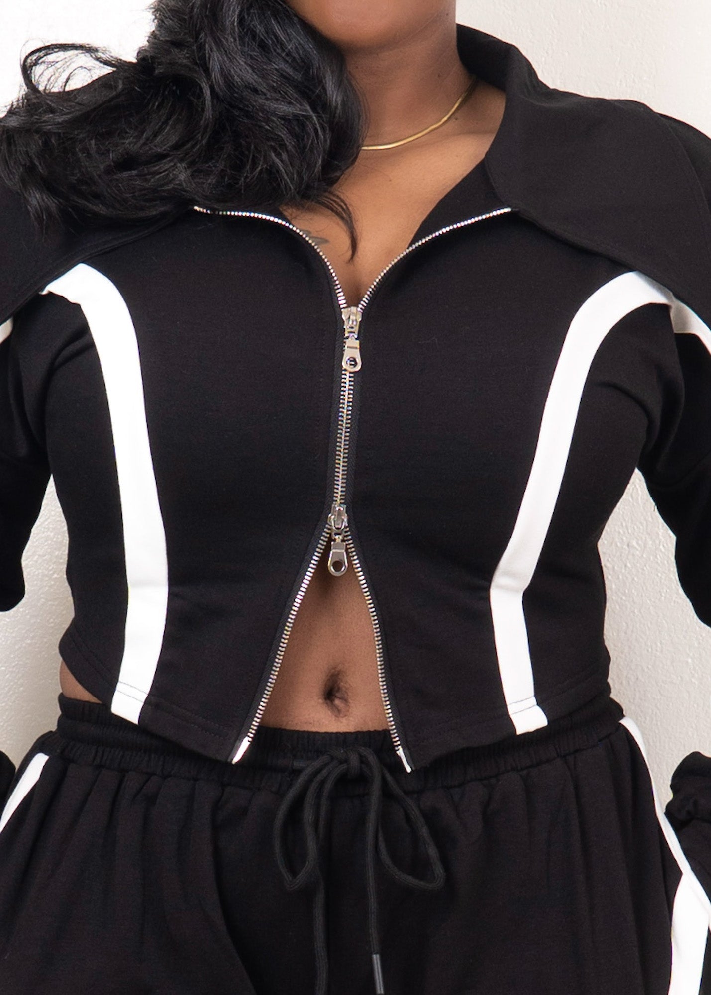 Black cropped zip-up track jacket with white contrast piping, fitted silhouette, and adjustable zipper styling
