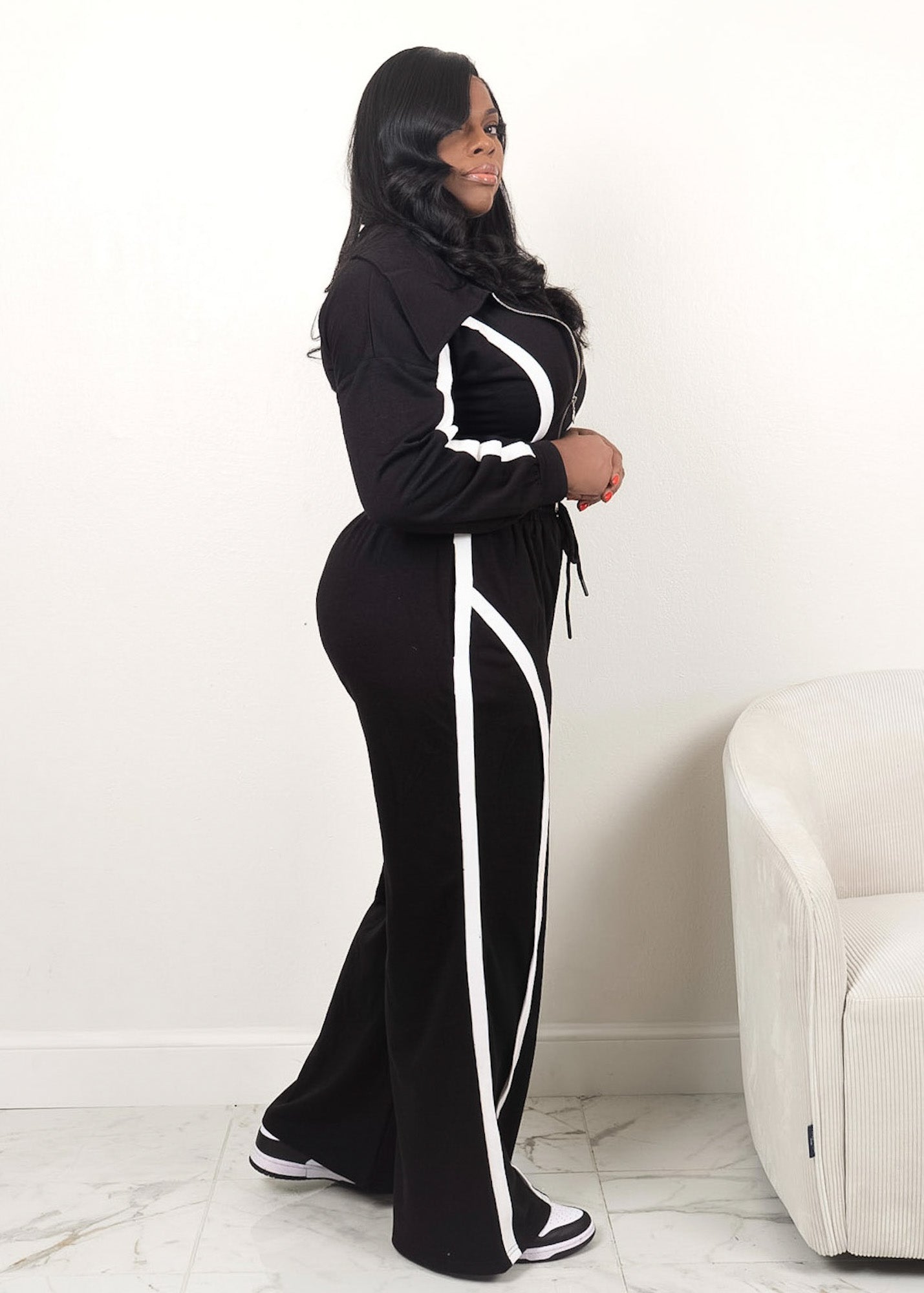 Black two-piece tracksuit with white contrast piping, fitted zip-up jacket and wide-leg pants shown in side profile
