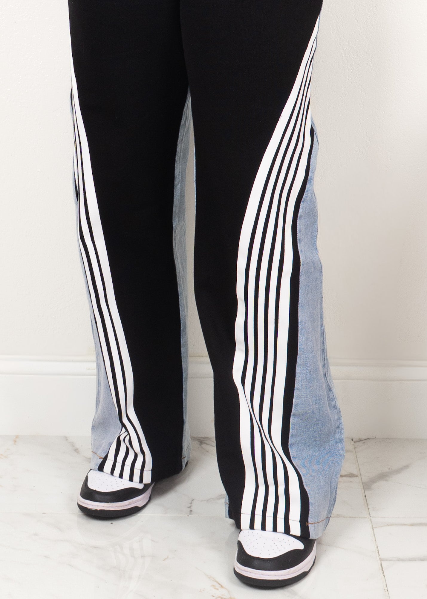 Black high-waisted wide-leg track pants with white stripe detailing and denim side panels styled with sneakers