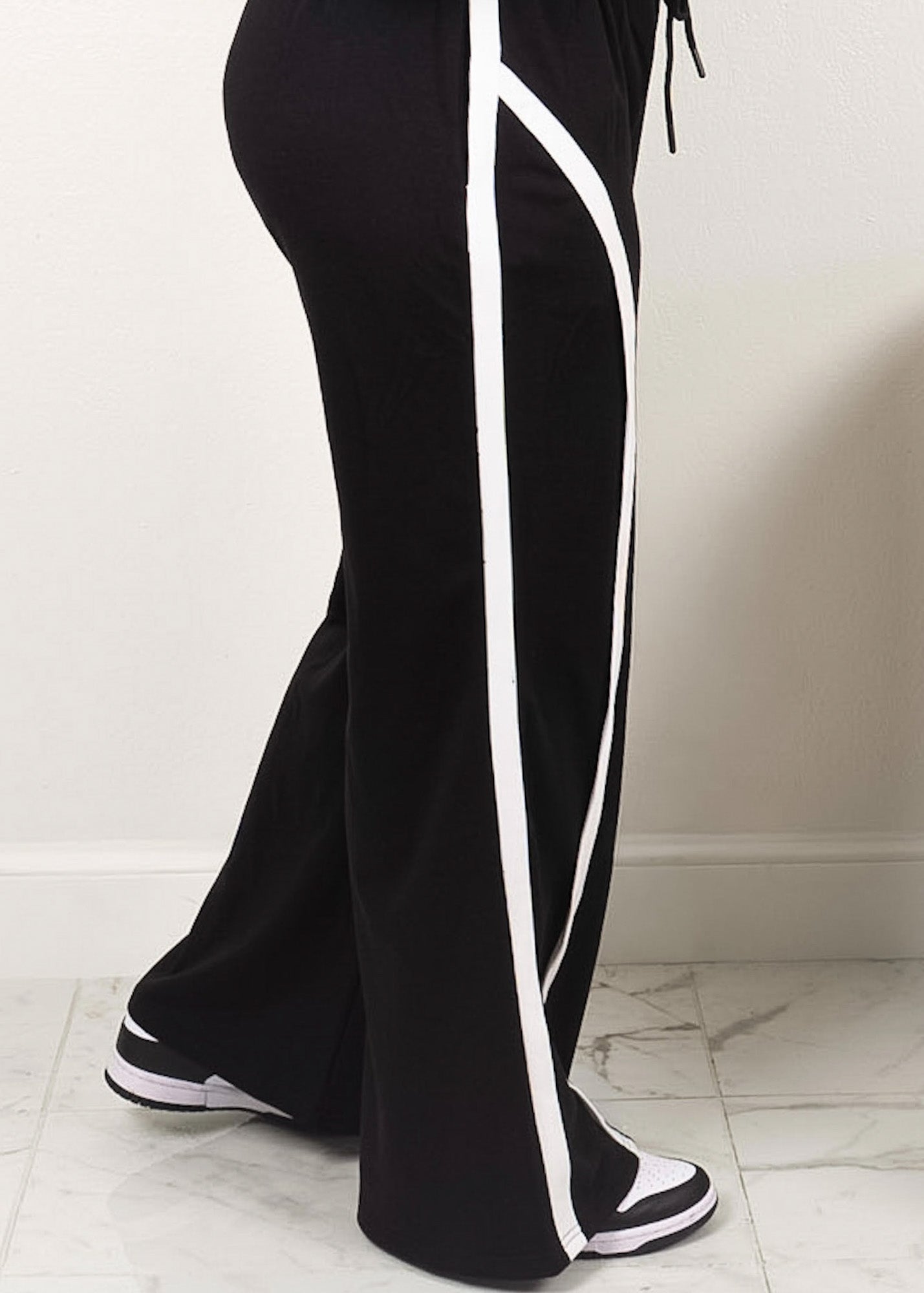 Black wide-leg track pants with white contrast piping, high-waisted fit, and sneaker-ready hem detail
