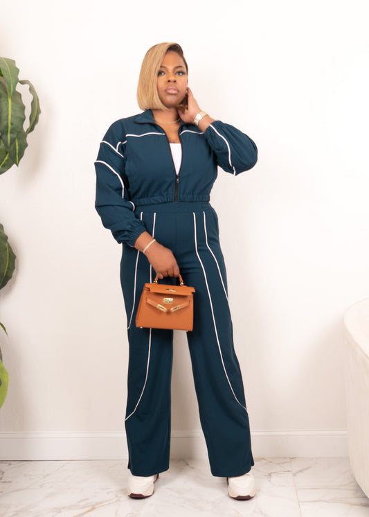 Model wearing hunter green and ivory contrast piping zip-up track set with wide-leg pants, full-body front view holding tan handbag