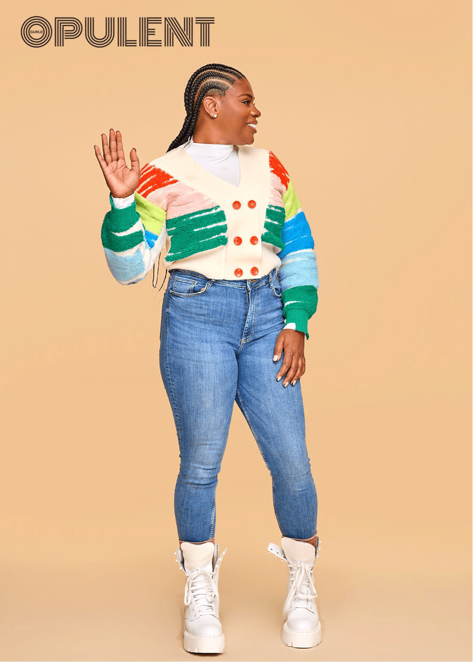 Model wearing a rainbow-striped cardigan and white turtleneck with blue skinny jeans and white boots, showcasing cozy cotton knitwear for fall.