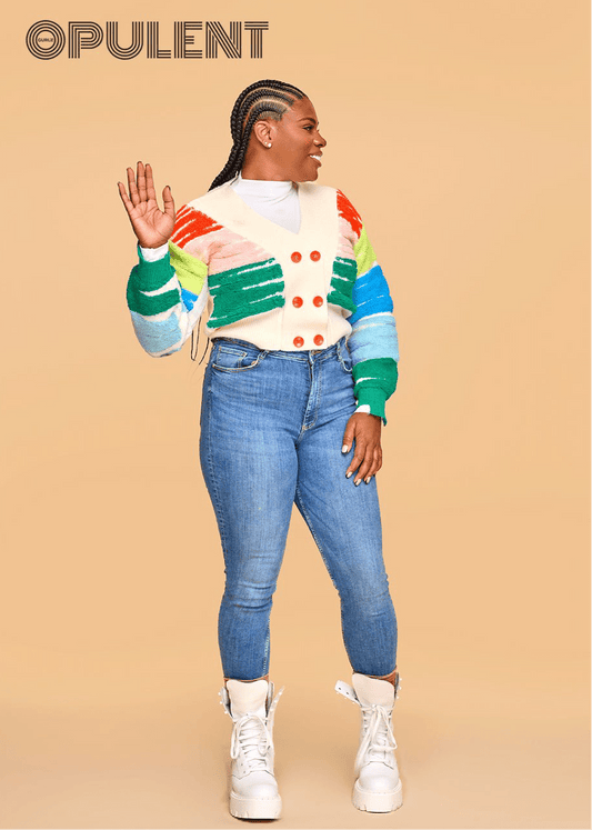 Model wearing a rainbow-striped cardigan and white turtleneck with blue skinny jeans and white boots, showcasing cozy cotton knitwear for fall.