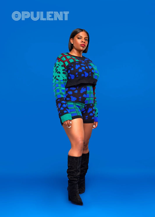 

Front view of Model wearing jungle sweater set with high-waisted knit shorts and bold green and blue print, paired with black boots