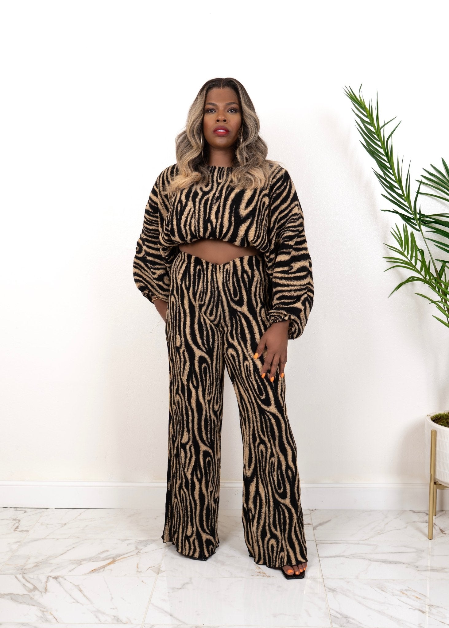 Model wearing The Wild Statement Set — long-sleeve crop top and wide-leg pants in black and tan abstract knit print, standing with one hand on hip