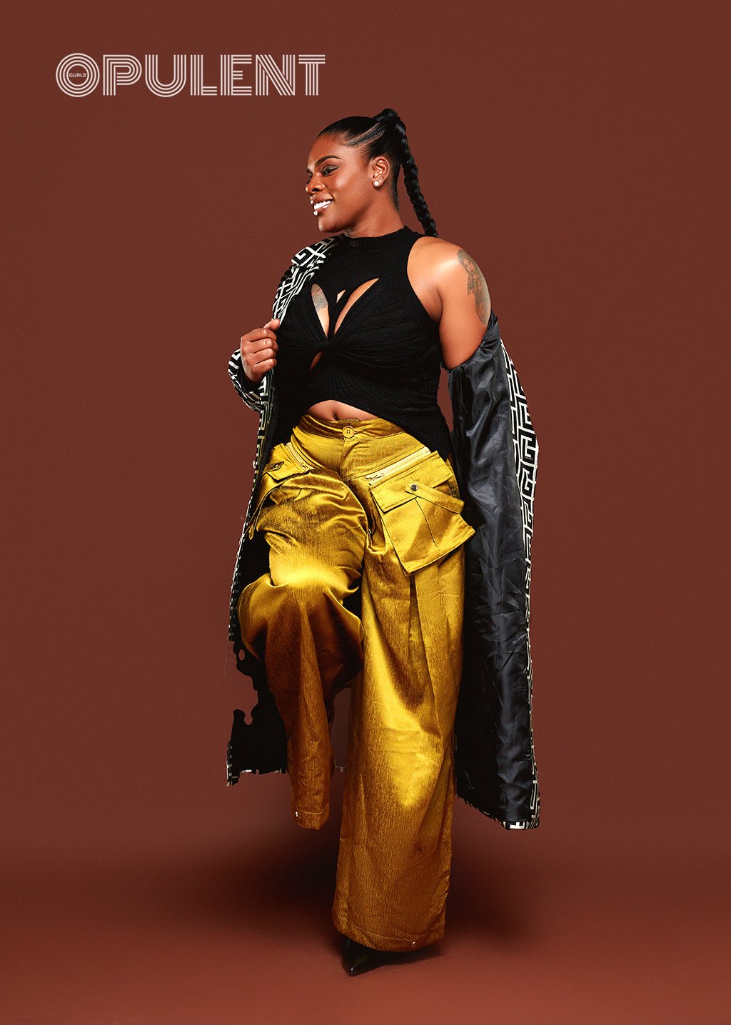 Sleeveless black twisted cutout sweater top styled with high-waisted gold metallic pants and a patterned coat, perfect for bold fall fashion looks.