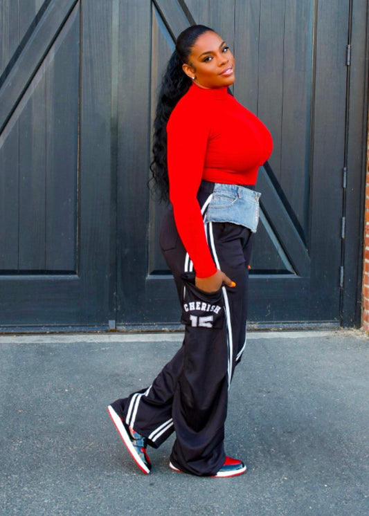 Woman wearing red long-sleeve top and black Very Forward Jean Sweats joggers with white lettering, standing outdoors by blue doors.