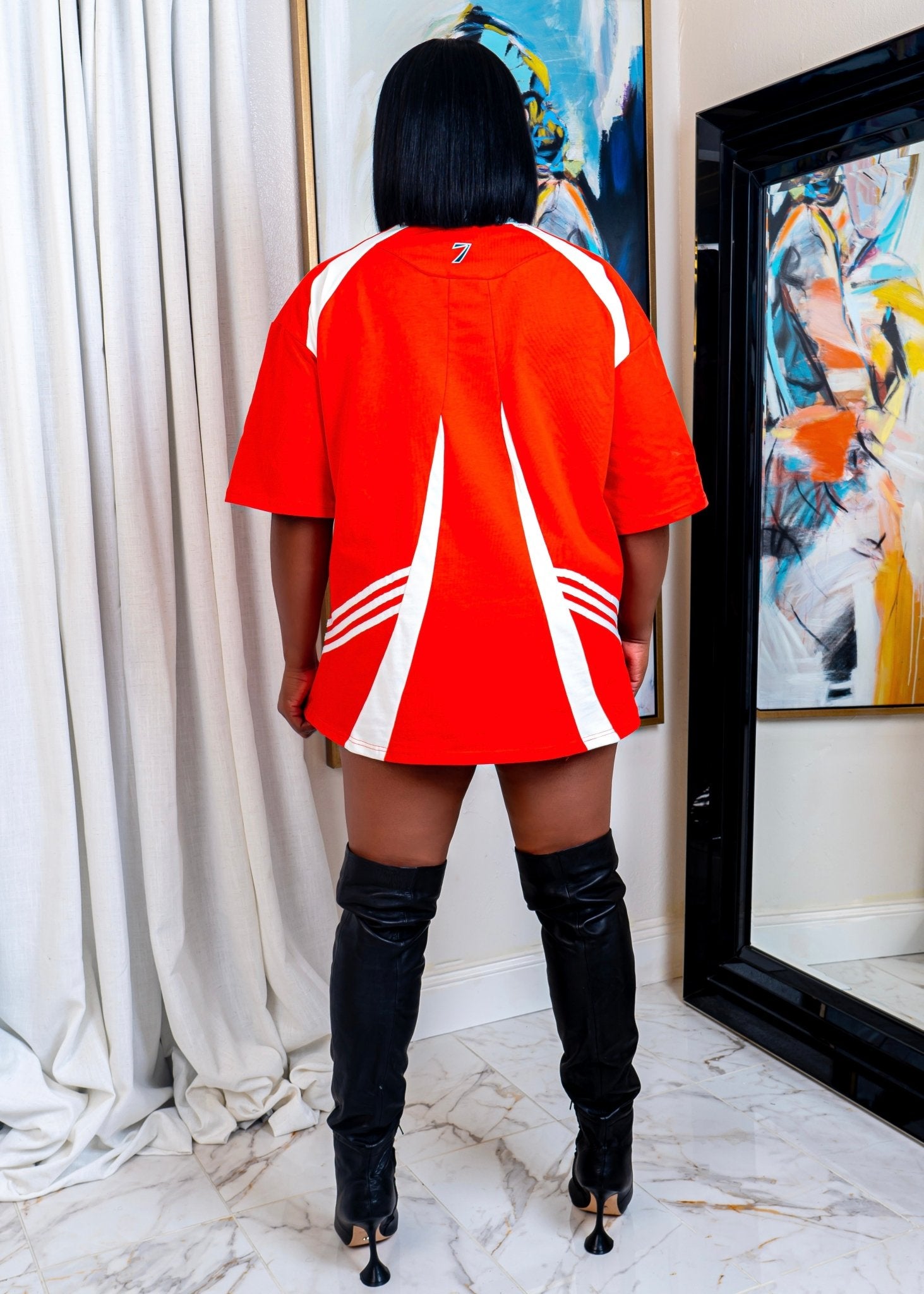 Back view of oversized red jersey dress with white stripes and relaxed fit – sporty streetwear mini dress styled with black thigh-high boots from Opulent Gurlz.
