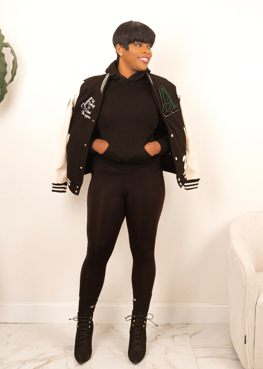 women’s black and white varsity jacket with letterman patches styled with leggings and heels for elevated streetwear look
